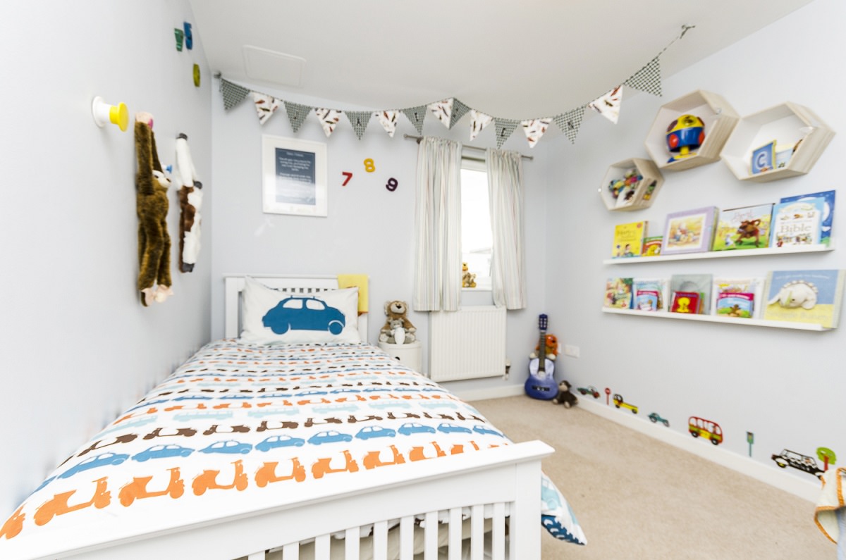 دکوراسیون اتاق خواب پسر بچه ای با دیوار آبی پاستلی که دارای روتختی ماشین و موتور، اعداد سه بعدی دکوری و قفسه شش ضلعی می باشد